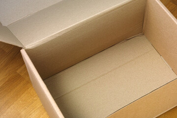 An empty open cardboard box on a wooden floor. Close up.