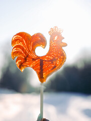 Cockerel candy. Russian lollipop against the backdrop of a winter landscape