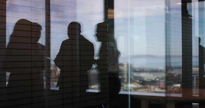 Business people, handshake and silhouette in corridor, shadow and walk for partnership, teamwork and window. Employees, paperwork and welcome with reflection, talking and planning in dark workplace