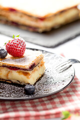 A piece of Napoleon cake with poppy seeds and cherries, decorated with strawberries, blueberries on a light background. Close up