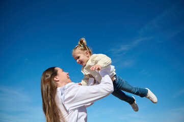 Bottom view of a happy harmonious family of a young loving caring mother throwing up her little...