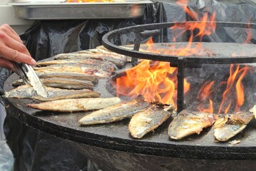 Grilled fish on a bowl-shaped flat grill with fire hole in the center. Outdoor seafood barbecue cooking. Picnic on backyard on open air. Street food concept. Preparing fish over open campfire