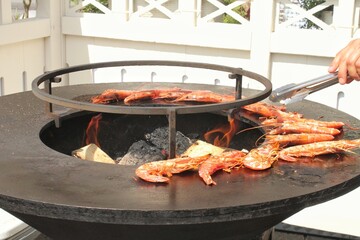 Seafood slices are cooked on a fire pit surface in the shape of cone shaped bowl. Bowl-shaped flat...