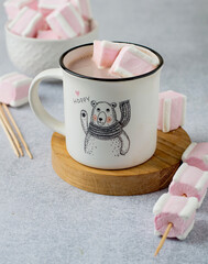A fun patterned cocoa cup with white and pink marshmallows on a wooden stand.