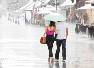 Couple under umbrella walking in heavy summer rain - 703538788