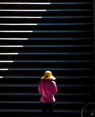 One woman wearing yellow hat walking up the public stairs in sunlight and shadows - 703538794