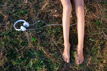 Bare female legs on a grass and headphones - 703540595