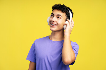 Portrait of smiling attractive boy teenager with dental braces, listening music in wireless...