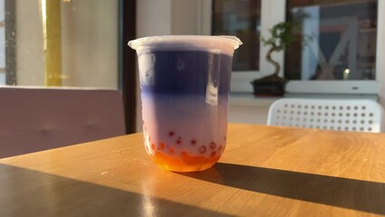 Bubble Tea with orange balls Lilac blue drink on wooden table on a sunny street