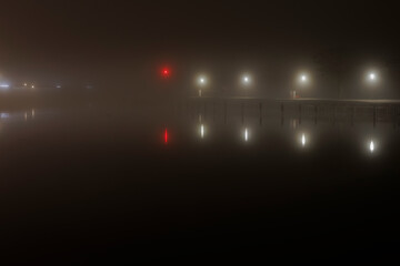 Mooring in the harbour for boats, dark and foggy picture, the lights reflect in water