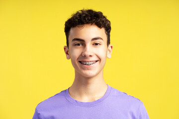 Closeup portrait of smiling confident  boy with dental braces on teeth looking at camera isolated on yellow background. Health care, orthodontic concept - obrazy, fototapety, plakaty