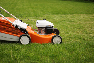 Close up orange-grey electric lawn mower on bright lush green lawn. Gardening work tools. Rotary lawn mower machine cut grass. Professional lawn care service. Place for text