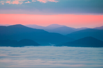A sea of fog and silhouettes of mountains on the background of the sky in the colors of the sunrise