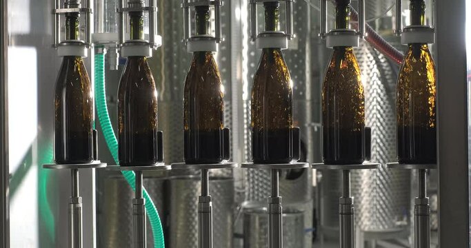 Glass bottles filled up with red wine. Private wine factory. Filling wine by the machine into bottles. Wine bottling production line. Slow motion