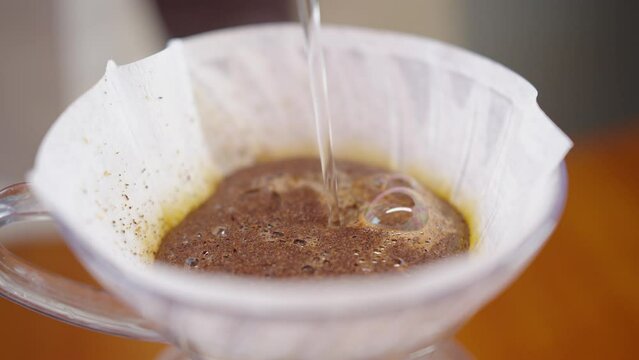 Brewing coffee with the v60 method. Water is poured from a kettle into a glass cup through a coffee filter, water is mixing with ground coffee beans