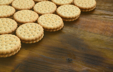A round sandwich cookie with coconut filling lies in large quantities on a brown wooden surface. Photo of edible treats on a wooden background with copy space