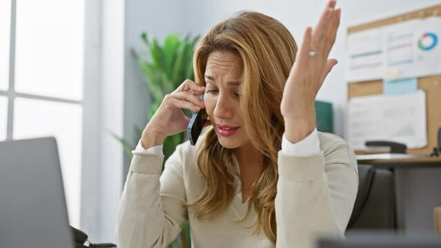 Worried woman on phone in office displaying anxiety and stress while working indoors at her workplace.