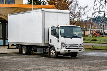 Cab over white compact semi truck with long box trailer deliver cargo to local business and...