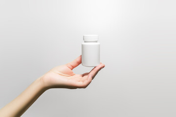 hand holding a white plastic jar with pills