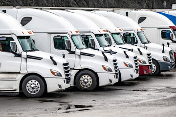White big rig pro semi truck tractors with semi trailers standing in row on the industrial parking...