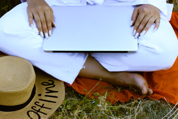 Girl in white luxury clothing sits on green grass with laptop on a knees at summer. Remote job, work online. Straw hat with text OFFLINE. Rich woman.