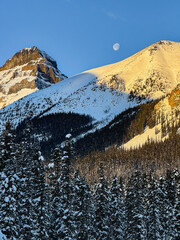 Moon peaking behind snowy mountains