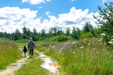 Naklejka na ściany i meble Mother and child walking on countryside path with muddy puddles in summer