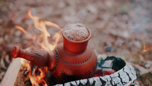 Old clay coffee pot on camping fire or on coals. The concept of adventure, travel, tourism and camping. Traditional process boil Turkish coffee