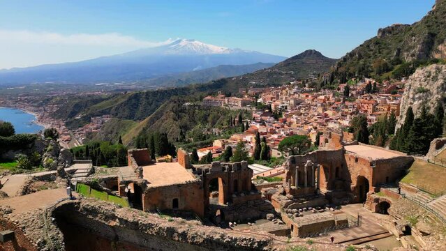Taormina, Sicily, Italy. Cityscape drone aerial view. Old Greek theatre ruins with active eruption volcano Etna background. Popular travel destination in Europe, UNESCO historical heritage