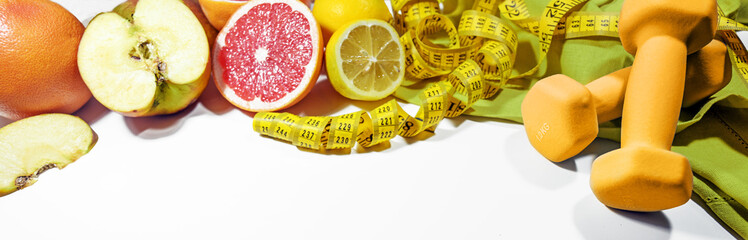 Lose weight with healthy eating, fitness and control, symbolized by fresh fruits, dumbbells and a measuring tape on a light gray background, wide panoramic format, copy space - obrazy, fototapety, plakaty