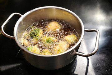 Beer battered cauliflower and broccoli are deep fried in a pot with hot boiling oil on a black...