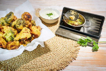 Deep fried cauliflower and broccoli in beer batter ready to eat on a wooden table and a smartphone showing how to cook the recipe, copy space, selected focus