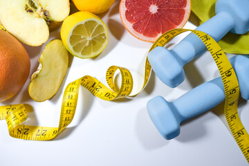 Healthy lifestyle, fitness and slimming symbolized by fresh fruits, measuring tape and dumbbells...
