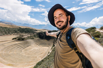 Happy young tourist man taking selfie portrait in Moray, agricultural terraces in Peru. Joyful tourist enjoying summer vacation in South America. - obrazy, fototapety, plakaty