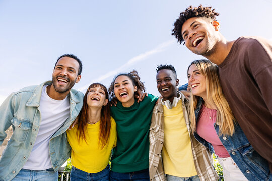 Young group of people having fun together outdoors in a sunny day. Multiracial best friends bonding enjoying time together at city street. United millennial students laughing.