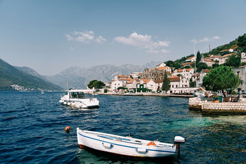 Fototapeta na wymiar White fishing boat is moored at a pier near the shore of Perast. Montenegro