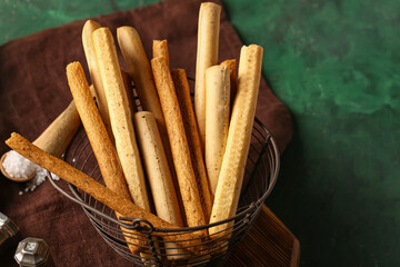 Basket with tasty Italian Grissini on green background, closeup