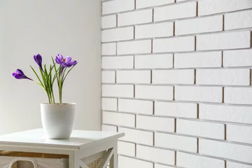 Gordijnen Pot with beautiful crocus flowers on end table near white brick wall © Pixel-Shot