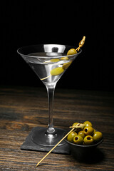 Glass of tasty martini and green olives on dark wooden table