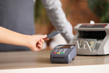 Young woman paying with credit card via banking terminal in shop, closeup