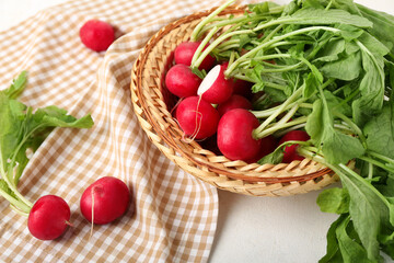 Wicker basket of ripe radish with green leaves on light background