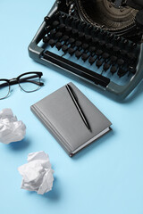 Vintage typewriter with crumpled paper, eyeglasses and notebook on blue background
