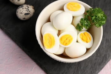 Board with bowl of boiled quail eggs on lilac background