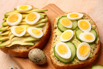 Tasty toasts with quail eggs, avocado and cucumber on light wooden background, closeup