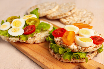Fototapeta na wymiar Rice crackers with quail eggs, tomatoes and lettuce on light wooden background, closeup