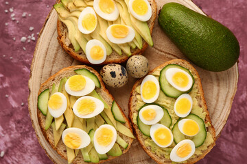 Obraz na płótnie Canvas Tasty toasts with quail eggs, avocado and cucumber on pink background, closeup