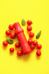 Bottle of ketchup and tomatoes on yellow background