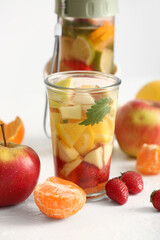 Glass and sports bottle of infused water with different sliced fruits on white table
