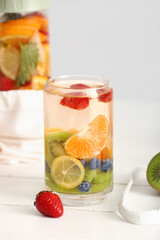Glass and sports bottle of infused water with different sliced fruits on white wooden table