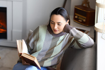 Young woman reading book on sofa near fireplace at home